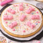 Easter Peeps sugar cookie pizza with marshmallow frosting, pink drizzle, pastel sprinkles, and Peeps bunnies on a marble surface.