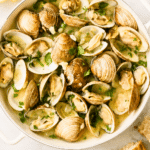 Drunken clams steamed in garlic butter beer broth in a white enamel pan with lemons and crusty bread