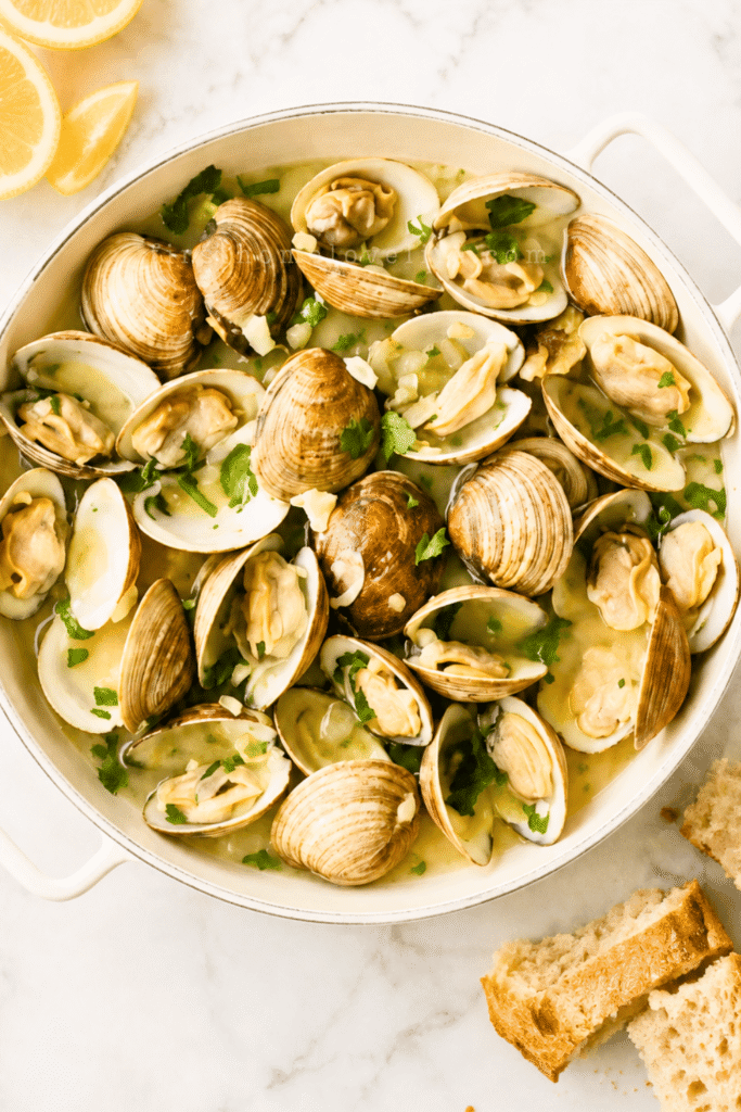 Drunken clams steamed in garlic butter beer broth in a white enamel pan with lemons and crusty bread