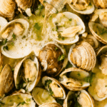 Pouring pale lager into littleneck clams with garlic and butter in a white enamel pan