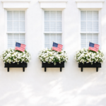 Simple patriotic window boxes with white flowers and American flags beneath matching white windows