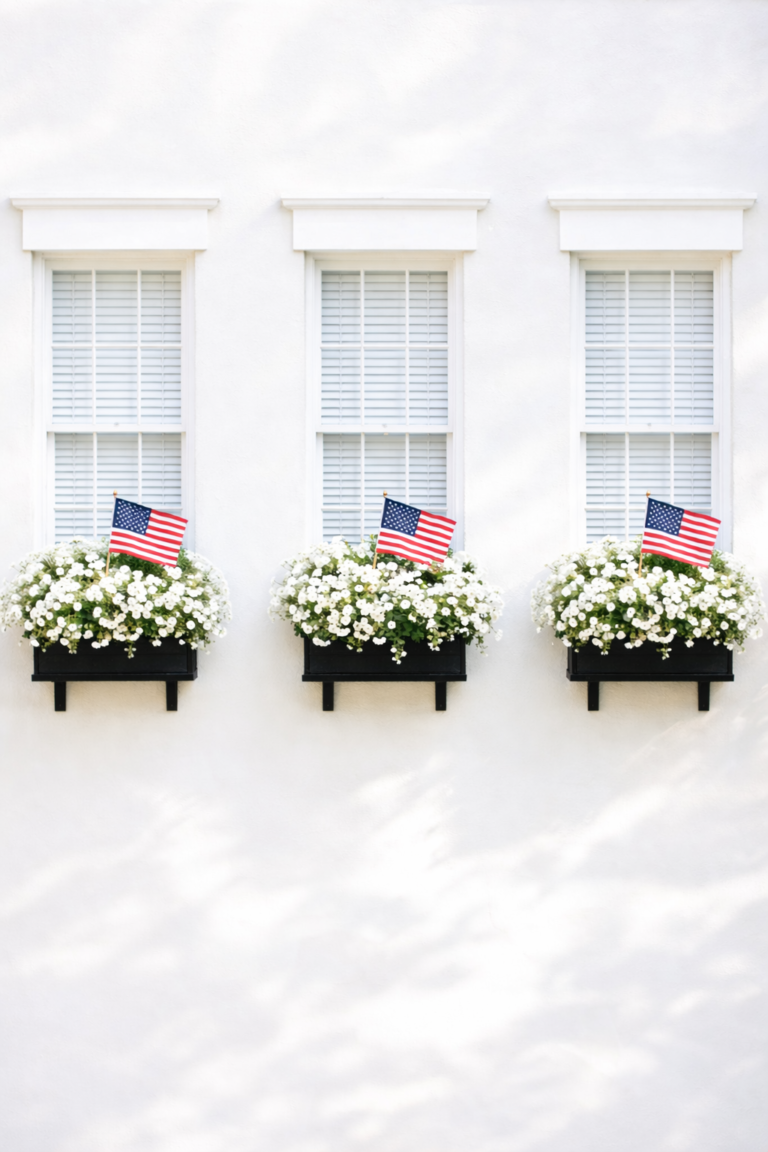 Simple patriotic window boxes with white flowers and American flags beneath matching white windows