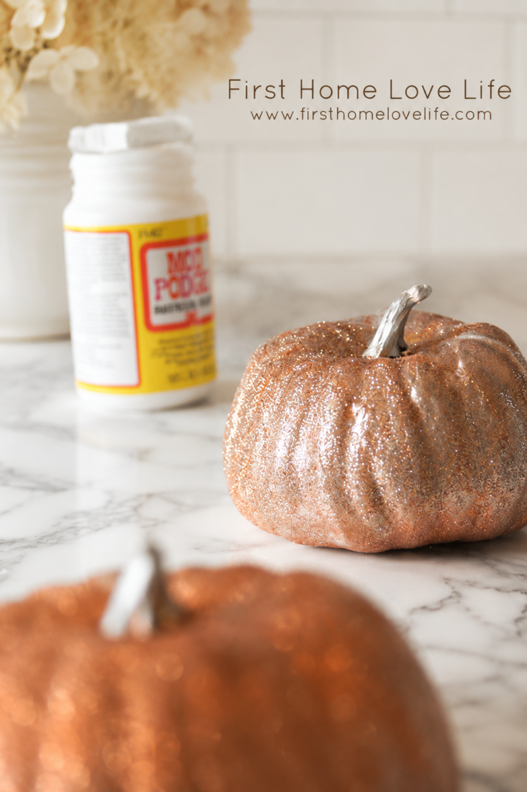 DIY glitter pumpkin craft on a white marble countertop with copper glitter pumpkins and fall decorating supplies.
