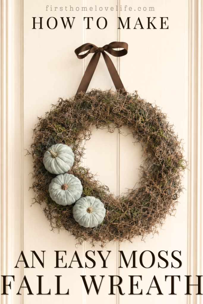 Blue pumpkin and moss fall wreath hanging from a brown ribbon on a creamy white paneled door.