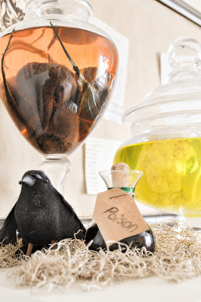Vintage Halloween poison bottle displayed beside specimen jars filled with preserved vegetables and spooky apothecary decor on a bright farmhouse-style mantel.