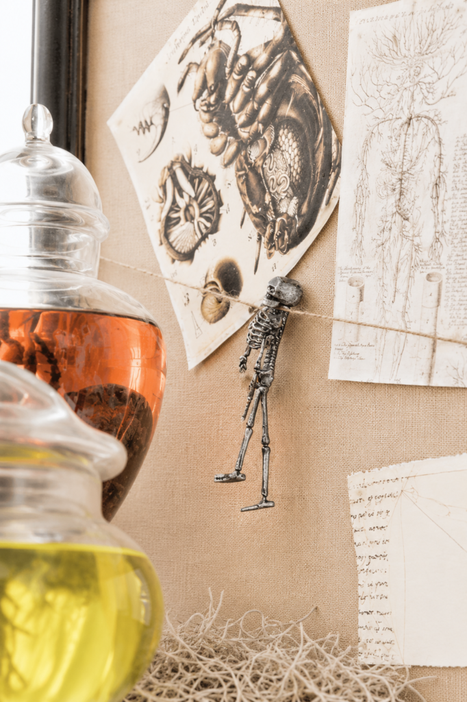 Vintage anatomy sketches and skeleton garland displayed above colorful specimen jars on a bright farmhouse-style mad scientist Halloween mantel.