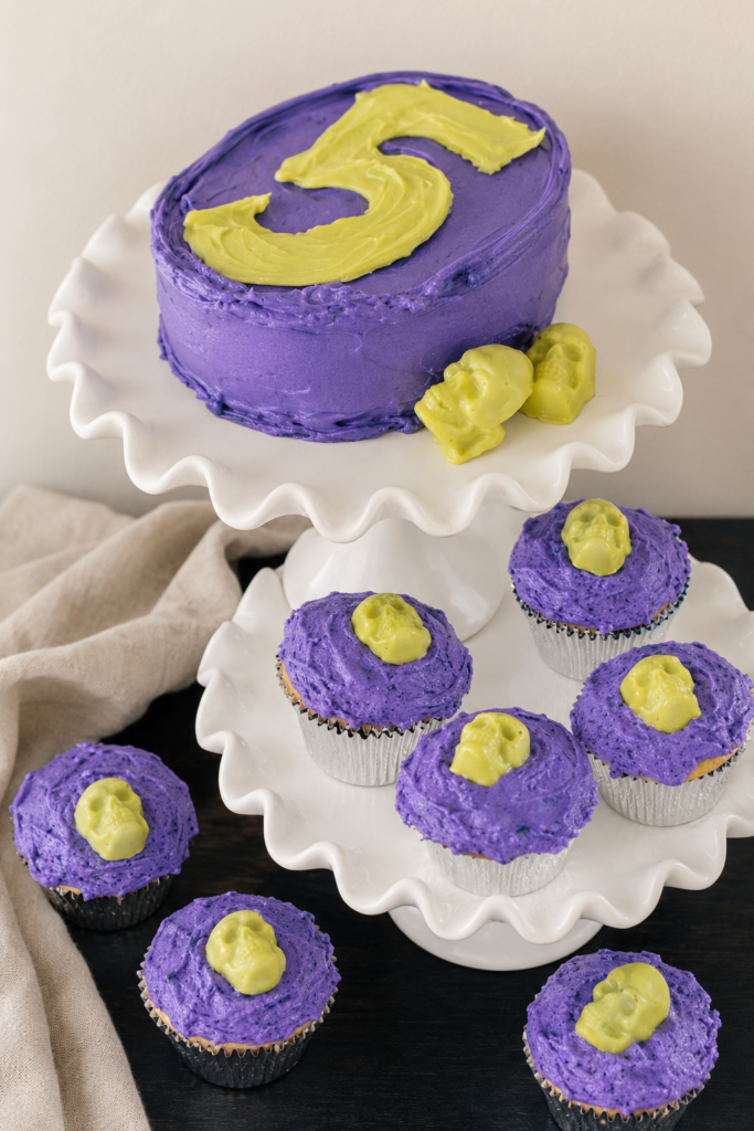 Purple witch-themed Halloween birthday cake with a green number five and matching cupcakes topped with green chocolate skulls