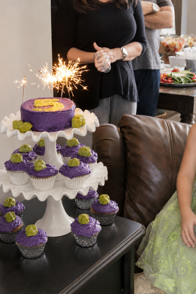 Purple witch-themed Halloween birthday cake with a green number five, sparkling candles and matching skull cupcakes