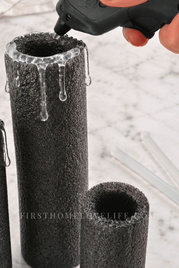 Using a low-temperature hot glue gun to create melted wax drips on black pool noodle Halloween candles.