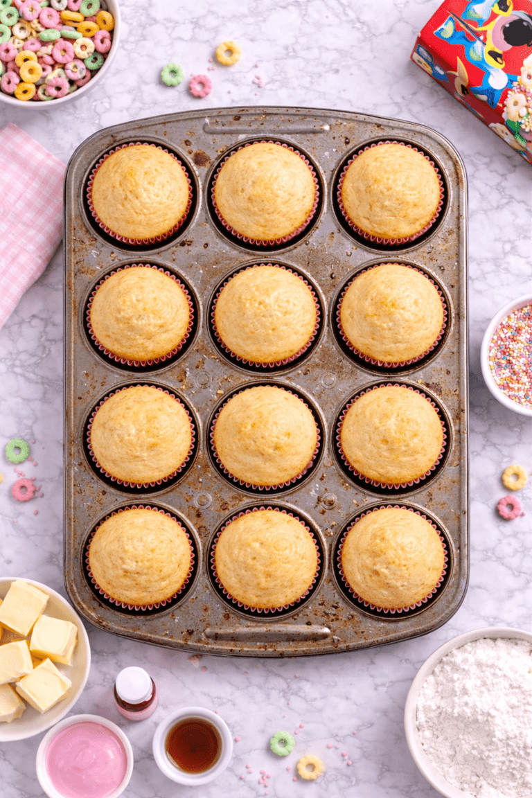 Unfrosted cereal milk cupcakes baked in a used muffin pan shown in a flat lay view on a marble countertop