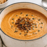 Creamy sweet potato soup in an off-white enameled cast iron Dutch oven topped with caramelized onions and fresh thyme