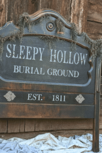 Thrifted headboard transformed into a Sleepy Hollow Burial Ground Halloween sign leaning against a rustic barn