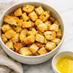 bowl of homemade garlic croutons on marble counter with neutral linen cloth