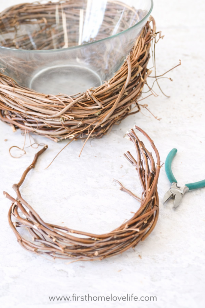 Grapevine wreath wrapped around a glass bowl to create a DIY bird’s nest vase on a light neutral surface