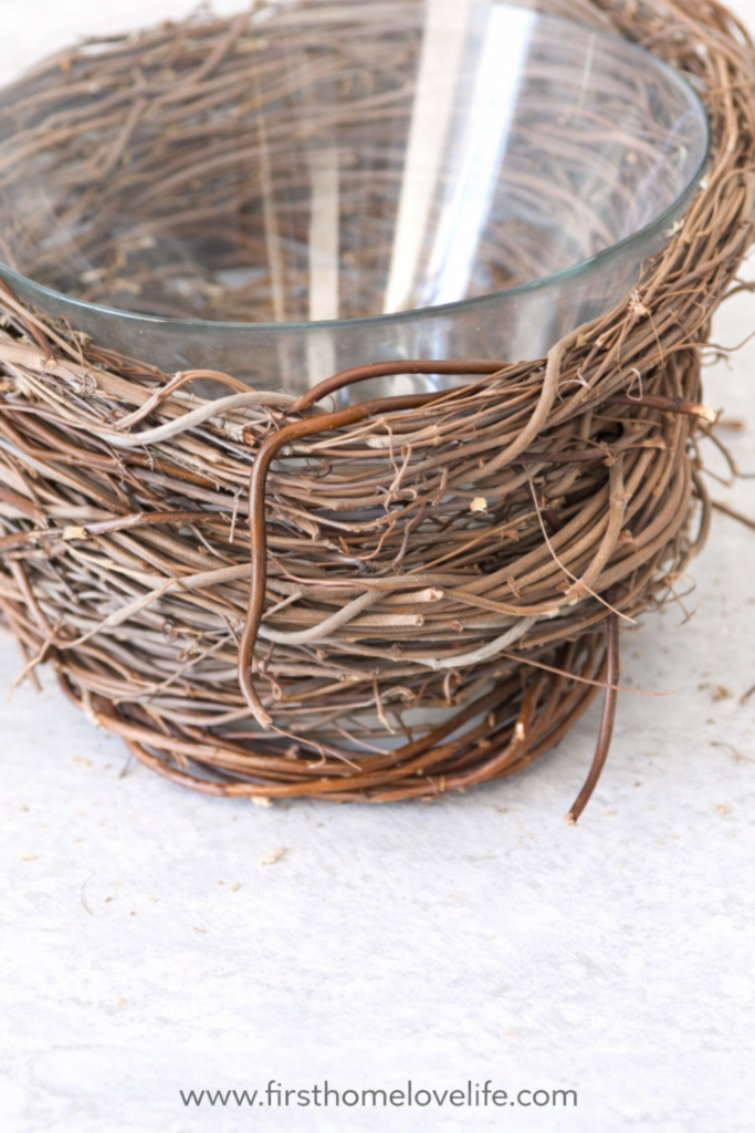 Close-up of a glass bowl wrapped with grapevine wreath pieces to create a DIY bird’s nest vase