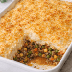Easy shepherd’s pie in a white baking dish with a slice removed showing layers of ground beef, vegetables, rich gravy, and creamy mashed potatoes.