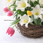 Spring birds nest vase filled with white lilies and pink tulips in a natural grapevine nest centerpiece on a light neutral background
