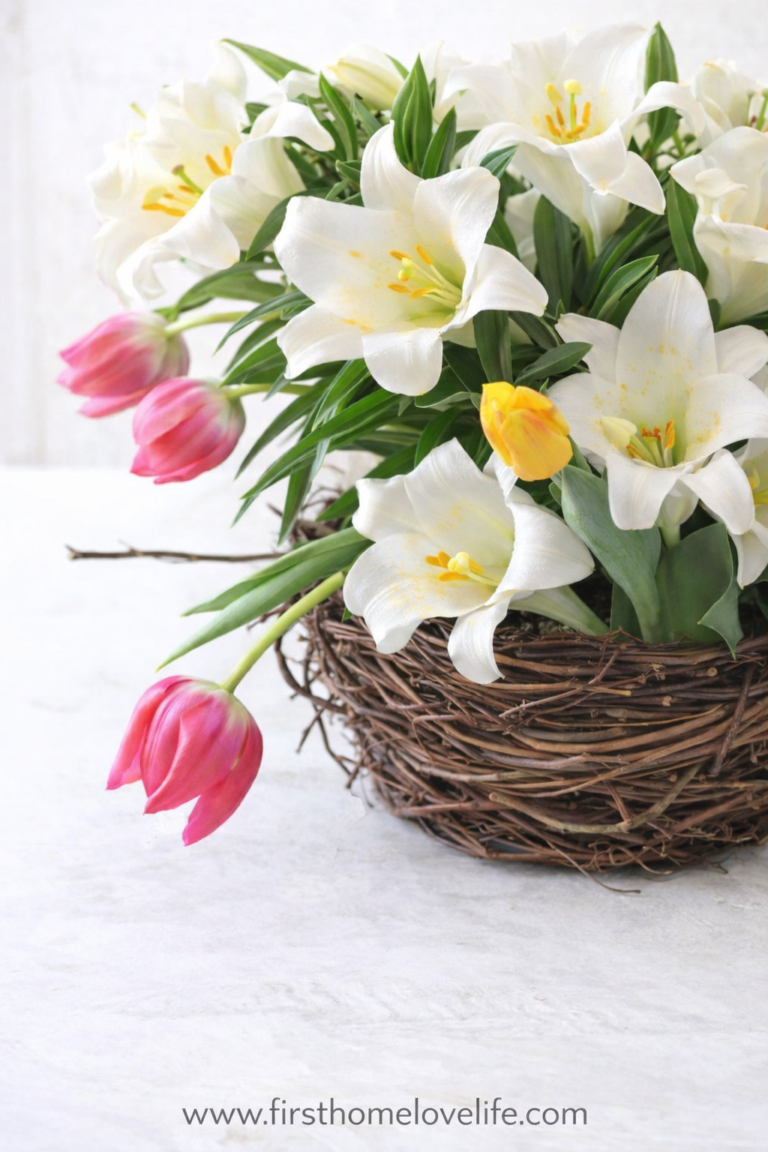 Spring birds nest vase filled with white lilies and pink tulips in a natural grapevine nest centerpiece on a light neutral background