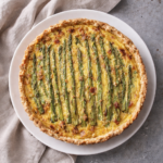 Ham asparagus and Gruyère quiche on a white plate with a neutral linen backdrop