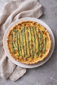 Ham asparagus and Gruyère quiche on a white plate with a neutral linen backdrop