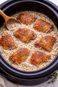 Crockpot creamy mustard chicken thighs in a black slow cooker with apple shallot cream sauce partially submerged