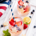 Patriotic Sparkler Sangria served in stemless glasses with strawberries, blueberries, apple stars, and sparkling wine on a white tray atop a marble countertop for a festive Fourth of July celebration.