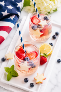 Patriotic Sparkler Sangria served in stemless glasses with strawberries, blueberries, apple stars, and sparkling wine on a white tray atop a marble countertop for a festive Fourth of July celebration.