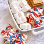 Patriotic red, white, and blue s’mores ingredients with swirled chocolate bark on a marble background