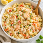 Creamy seaside pasta salad with shrimp, crab, rotini pasta, fresh vegetables, and lemon herb dressing served in a large white bowl on a marble countertop with a wooden spoon and neutral linen cloth.