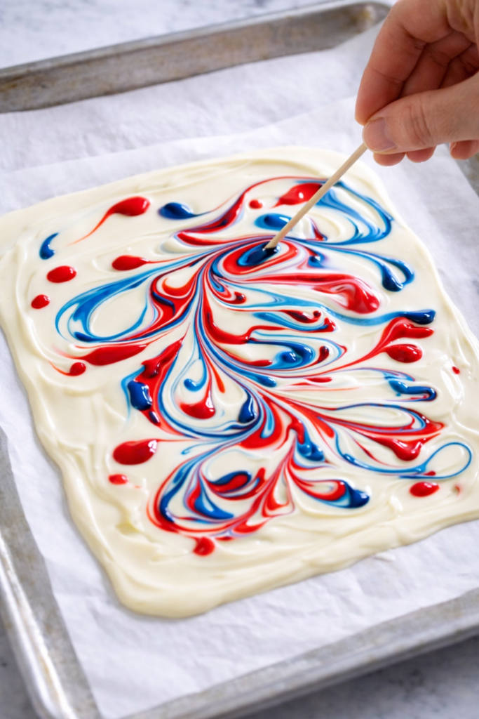 Swirling red, white, and blue food coloring into melted white chocolate on parchment paper