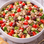 Greek grilled chicken salad in large white serving bowl with feta, olives, cucumbers, and tomatoes