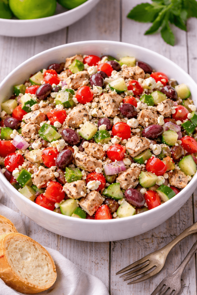 Greek grilled chicken salad in large white serving bowl with feta, olives, cucumbers, and tomatoes