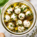 Bird's-eye view of homemade marinated mozzarella balls in a glass jar filled with garlic herb olive oil.