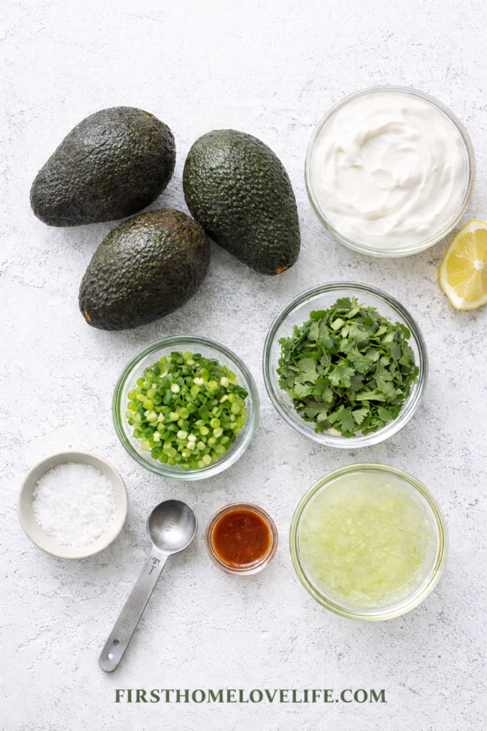 Flat lay of ingredients for freezer guacamole including avocados, lime juice, cilantro, green onions, sour cream, and salt
