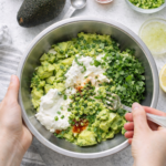 Mixing homemade freezer guacamole in a bowl with avocados, sour cream, cilantro, and lime juice