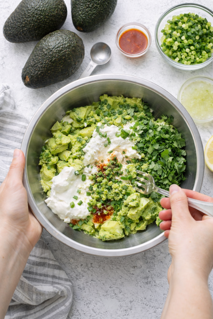 Mixing homemade freezer guacamole in a bowl with avocados, sour cream, cilantro, and lime juice