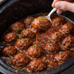 Spoon lifting a sriracha BBQ meatball from a crockpot with sauce dripping over homemade slow cooker meatballs