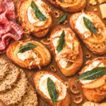 Squash butter crostini with ricotta, crispy shallots, and sage on a wooden charcuterie board with assorted cheeses, salami, and crackers.