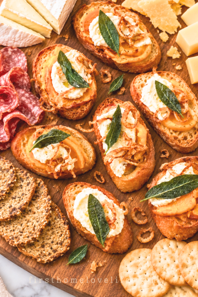 Squash butter crostini with ricotta, crispy shallots, and sage on a wooden charcuterie board with assorted cheeses, salami, and crackers.