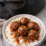 Bowl of rice topped with slow cooker sriracha BBQ meatballs and sauce with crockpot in the background