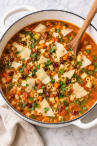 The best homemade minestrone soup in a white enamel Dutch oven topped with shaved Parmesan and fresh parsley on a marble countertop.