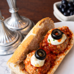 Close up of spooky turkey meatball sandwich with mozzarella and olive eyeballs on a white plate for an easy Halloween dinner idea.