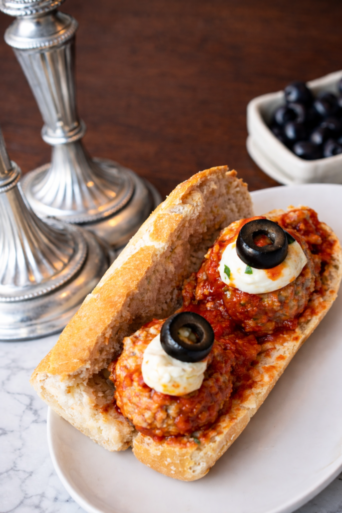 Close up of spooky turkey meatball sandwich with mozzarella and olive eyeballs on a white plate for an easy Halloween dinner idea.