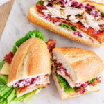 Leftover Thanksgiving turkey sandwiches on crusty hoagie rolls filled with roasted turkey, crispy bacon, smoked Gouda cheese, romaine lettuce, and cranberry mayonnaise.