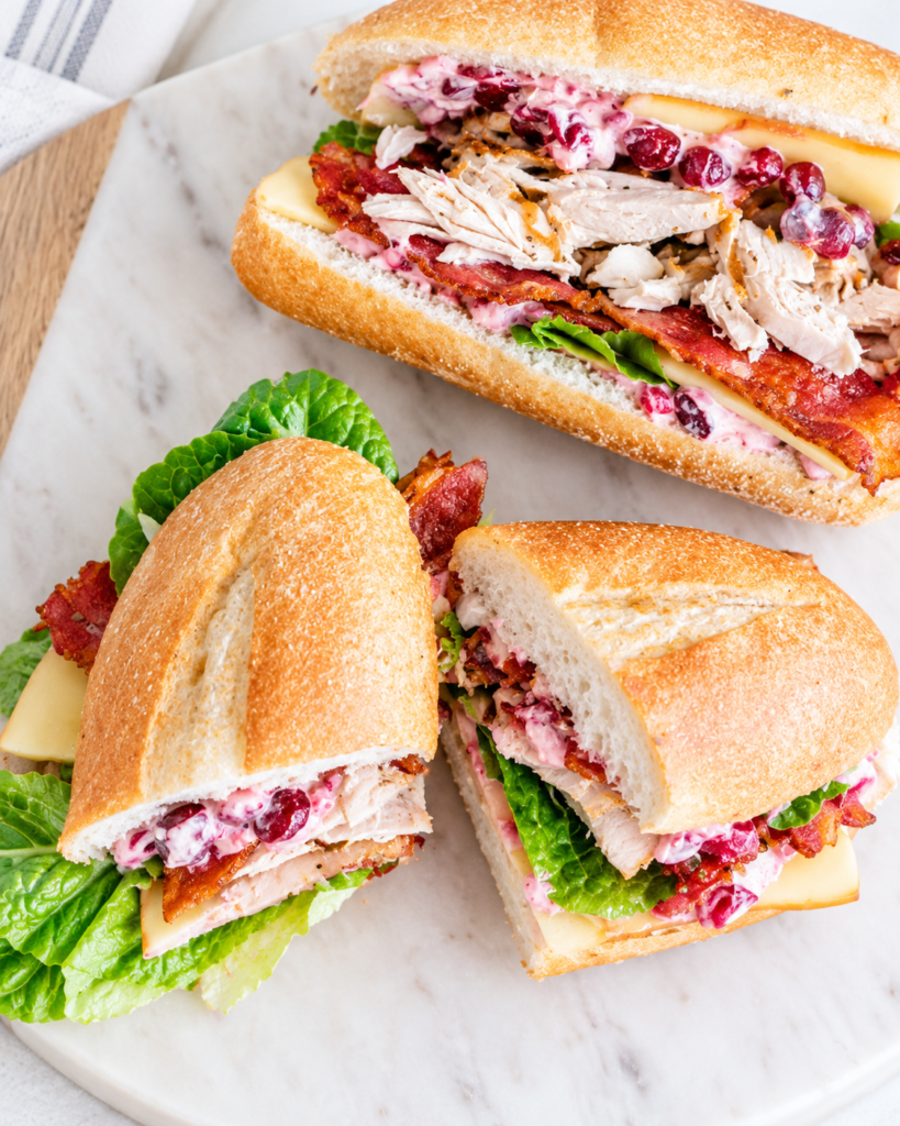 Leftover Thanksgiving turkey sandwiches on crusty hoagie rolls filled with roasted turkey, crispy bacon, smoked Gouda cheese, romaine lettuce, and cranberry mayonnaise.