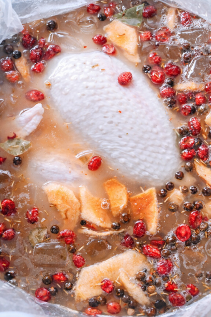 Raw turkey soaking in a brining bag with cranberries, citrus, herbs, and spices for Thanksgiving turkey brine