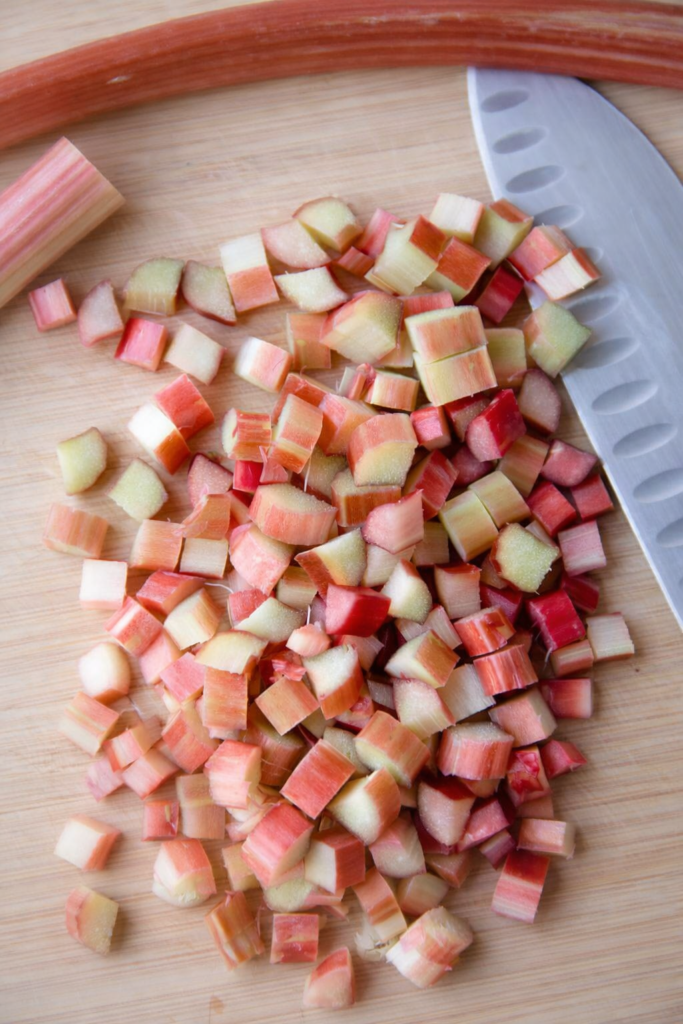Freshly chopped rhubarb pieces on a wooden cutting board with a kitchen knife