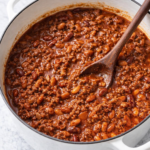 Hearty homemade chili with ground beef and beans in a white Dutch oven on a marble countertop
