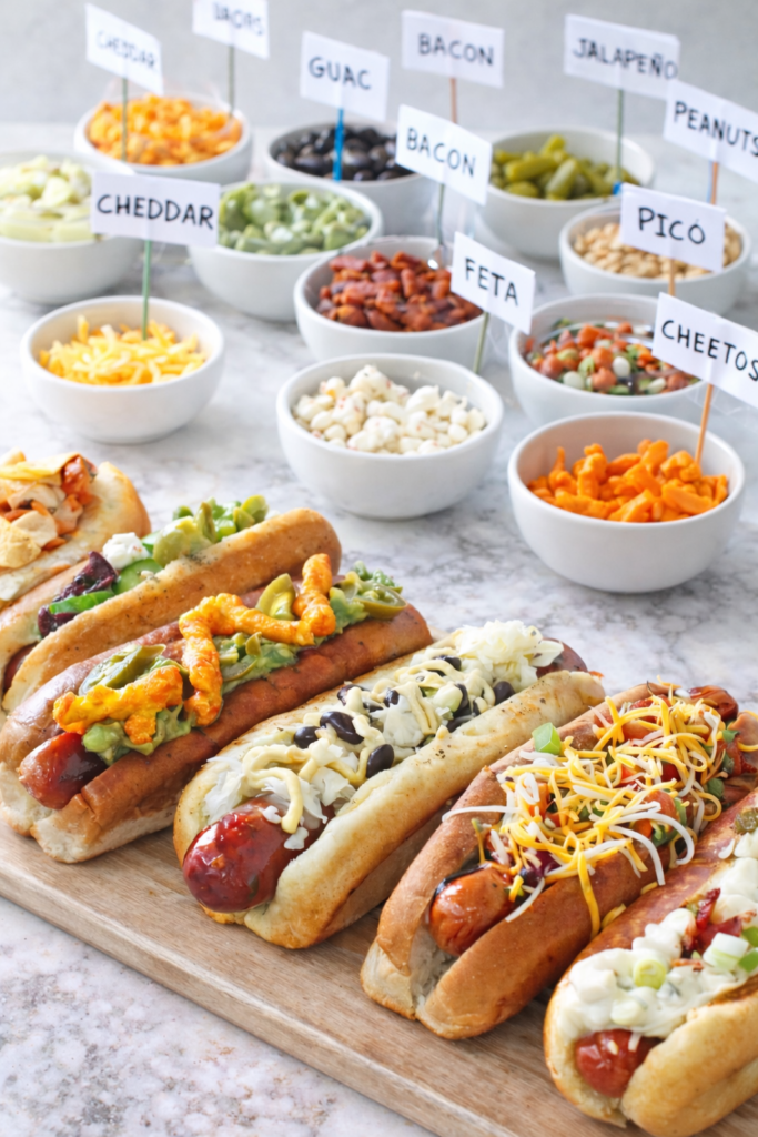 Gourmet hot dogs on a marble surface with assorted hot dog toppings served in white bowls, perfect for a build-your-own hot dog bar.