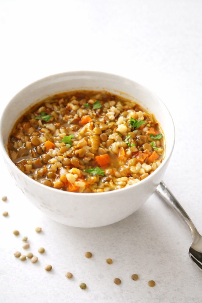 Bright bowl of lentil and brown rice soup with vegetables and herbs on a light background, cozy healthy homemade soup.